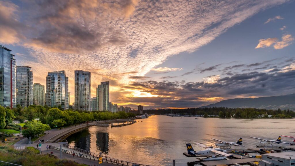 small planes moored in water at sunset with tall buildings and beautiful sky
